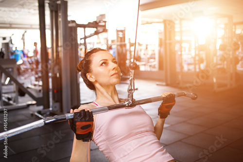 Young fitness woman performing close grip lat pulldown on cable machine photo