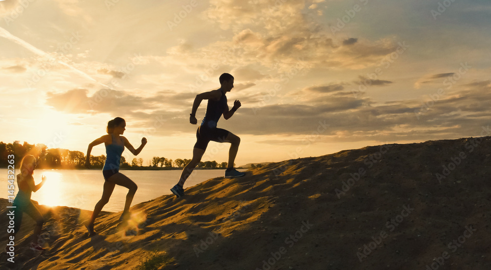 Sport motivations -group of athletes - two girls and a guy are fleeing the mountain, near river at dusk