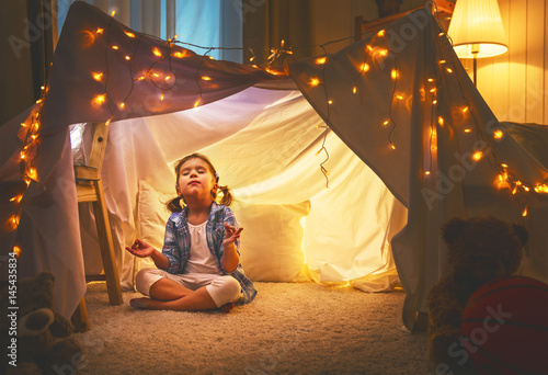 child girl playing meditates in yoga pose in tent at home © JenkoAtaman