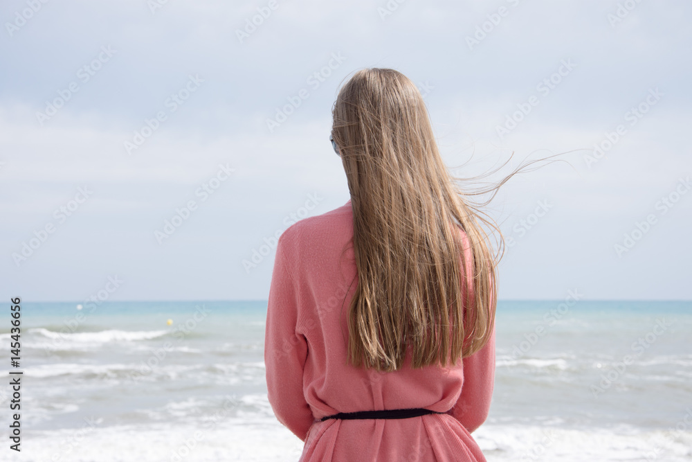 Obraz premium A lonely girl sitting on a bench by the sea and looking at the storm sea