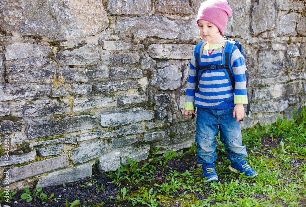 Boy with backpack standing near a stone wall. Boy with backpack standing near a stone wall.