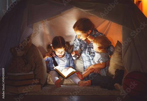 happy family mother and children reading a book in tent at home