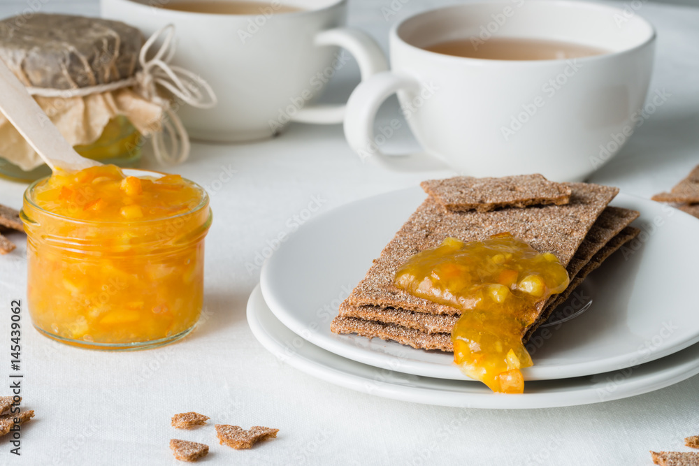 Brown rye crisp bread (Swedish crackers) with spread orange jam and cups of tea, on white background. Sweet snack or breakfast Brown rye crisp bread (Swedish crackers) with spread orange jam and cups of tea, on white background. Sweet snack or breakfast