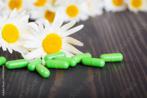 Capsules and chamomile flowers on wooden table. The concept of alternative medicine and phytotherapy.