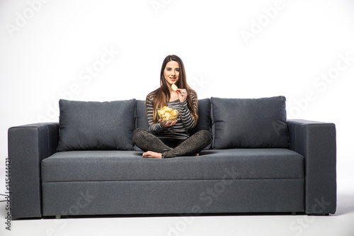 Young woman watching TV and eating chips sitting on sofa