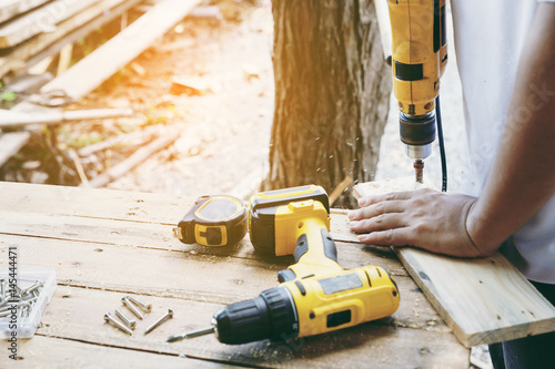 Carpenter's screwing a wood plate by wireless drill for make a chair, Diy at Home concept photo