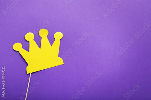 Yellow paper crown on stick on purple background photo