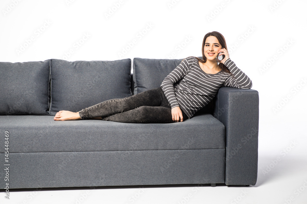 Happy young woman talking cell phone while lying on sofa on white Happy young woman talking cell phone while lying on sofa on white