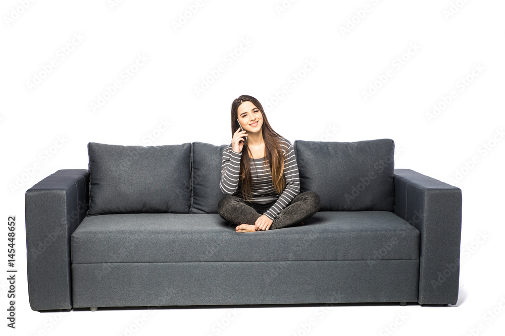 Obraz premium Happy young woman talking cell phone while sitting on sofa on white