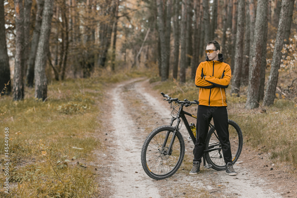 Young attractive man wears yellow suit on bike in the forest Young attractive man wears yellow suit on bike in the forest