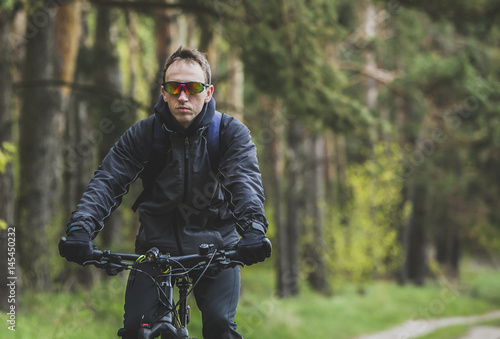 Young attractive man wears dark suit ride the bike on the forest road