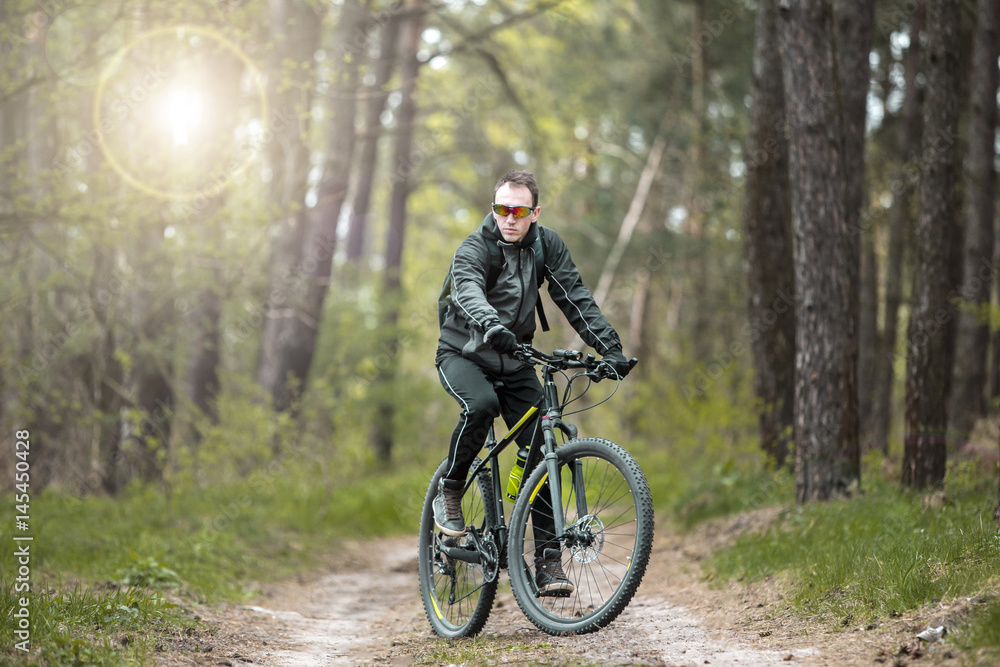 Young attractive man wears dark suit ride the bike on the forest road