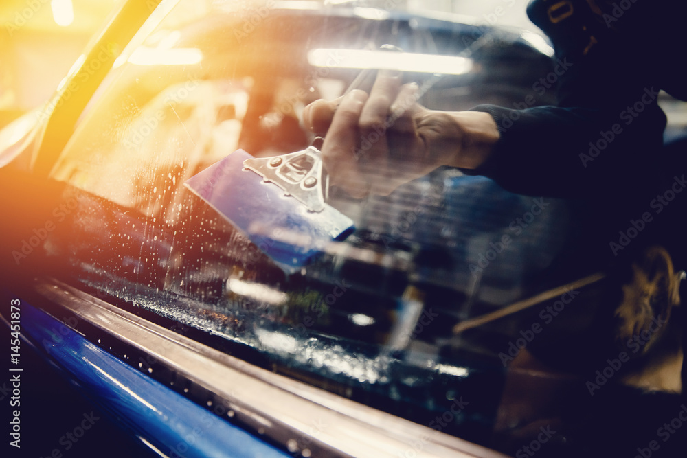 Φωτογραφία Master installs a tint film for the car glass with a hairdryer and spatula with glare of light