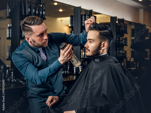 Hairdresser doing haircut to a bearded man in a barbershop.