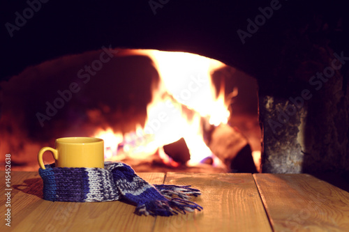warming pastime in the village/ Yellow mug in a blue scarf on the background of a retro fireplace 