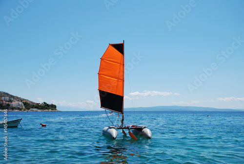 Inflatable catamaran with orange sail on the background of the sky and the sea