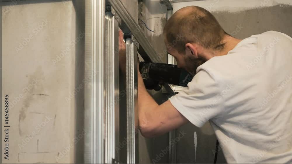 The worker drills the wall and fastens the frame The worker drills the wall and fastens the frame