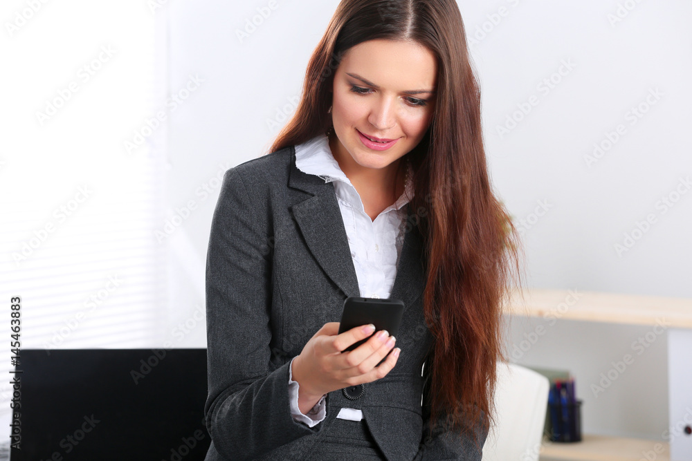 Businesswoman sending message with smartphone in office Businesswoman sending message with smartphone in office