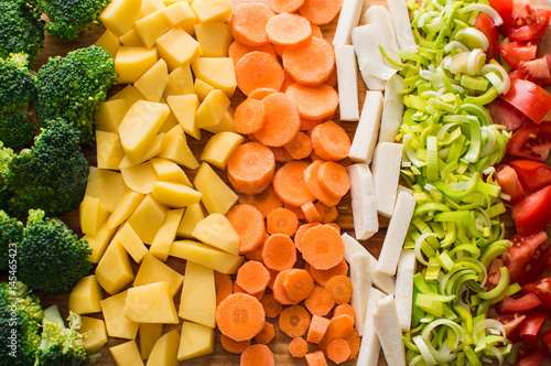 Sliced carrots, broccoli, parsley root, leek, tomato, potatoes on a wooden cutting board.