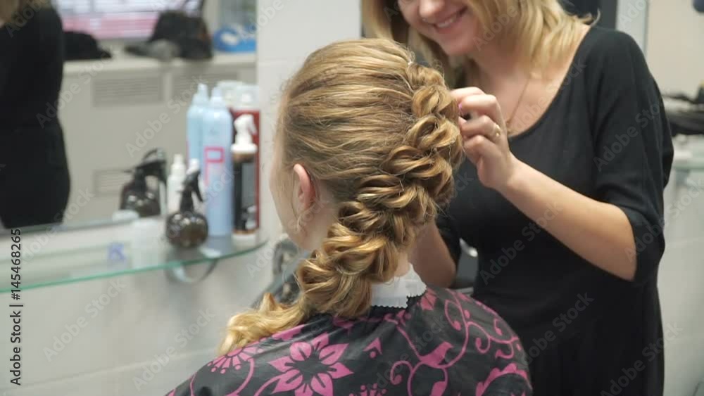 Portrait of a young woman in a beauty salon: creating a magnificent setting from curls. A blonde in a hairdresser does a beautiful hairstyle. Hair care and creating an image.