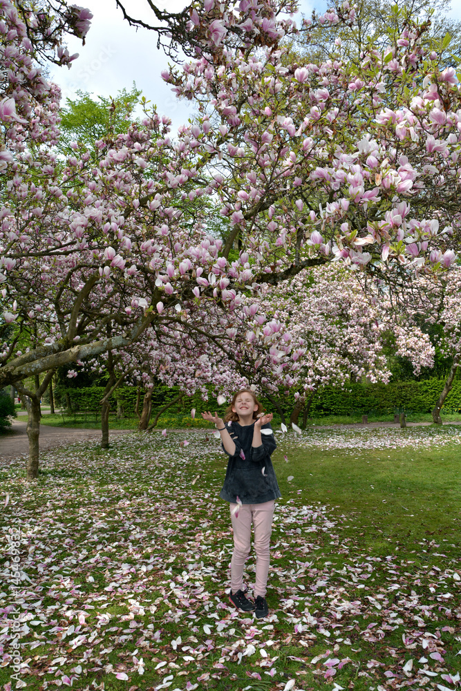 Mädchen wirft Magnolienblüten in die Luft, steht unter Bäume