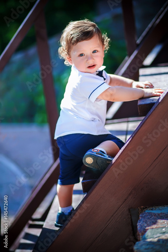 Little handsome boy climbs on the wooden stairs to the top.