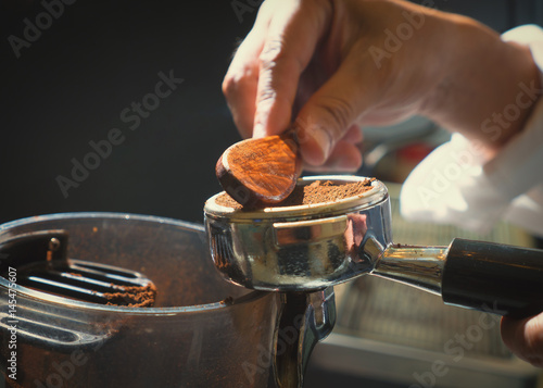 Barista pressing ground coffee into portafilter by tamper to making coffee