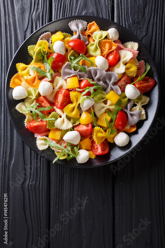 Warm salad of farfalle pasta, tomatoes, arugula and mozzarella closeup. Vertical top view photo