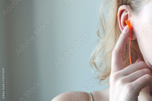 Blonde girl puts hand earplugs in ear closeup on white background