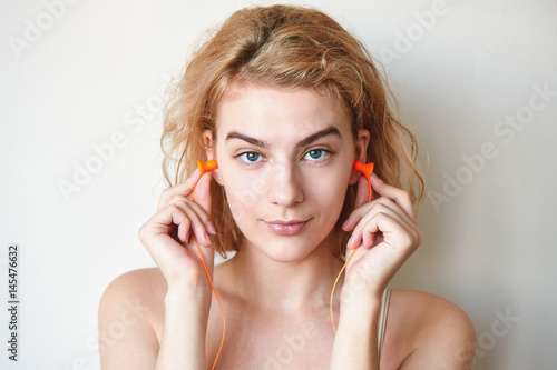 Photography Blonde girl puts earplugs in his ears on white background