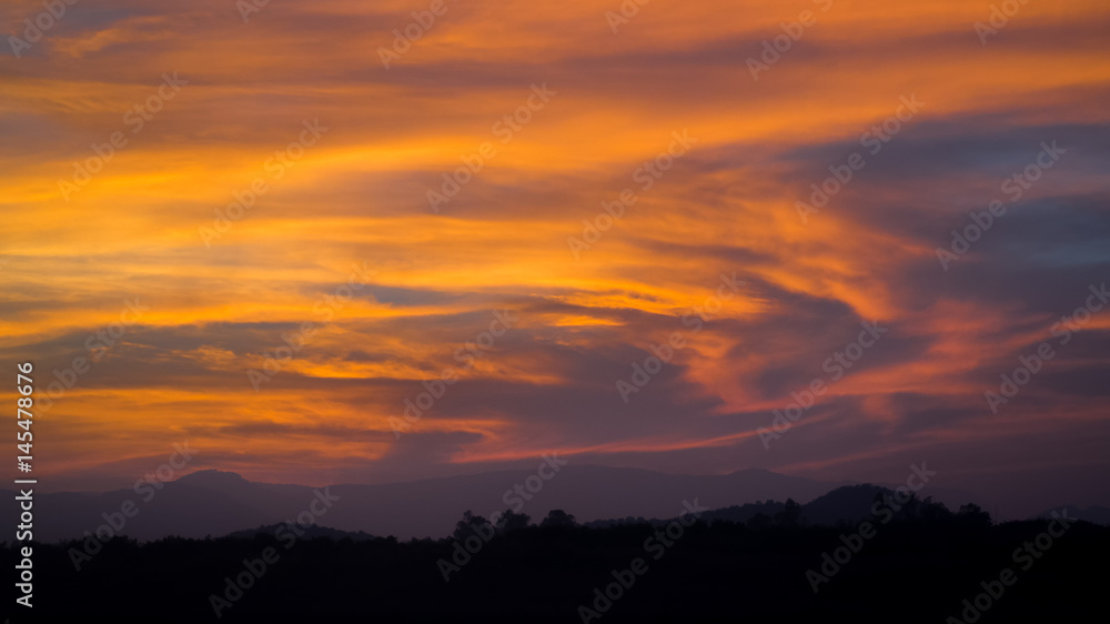 Dramatic sunset orange cloudy sky with tree and hill line silhouette Dramatic sunset orange cloudy sky with tree and hill line silhouette