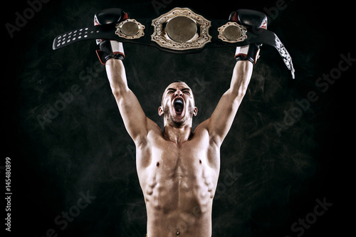 Fotografia Boxer with Champion belt celebrating flawless victory isolated on black background with copy Space