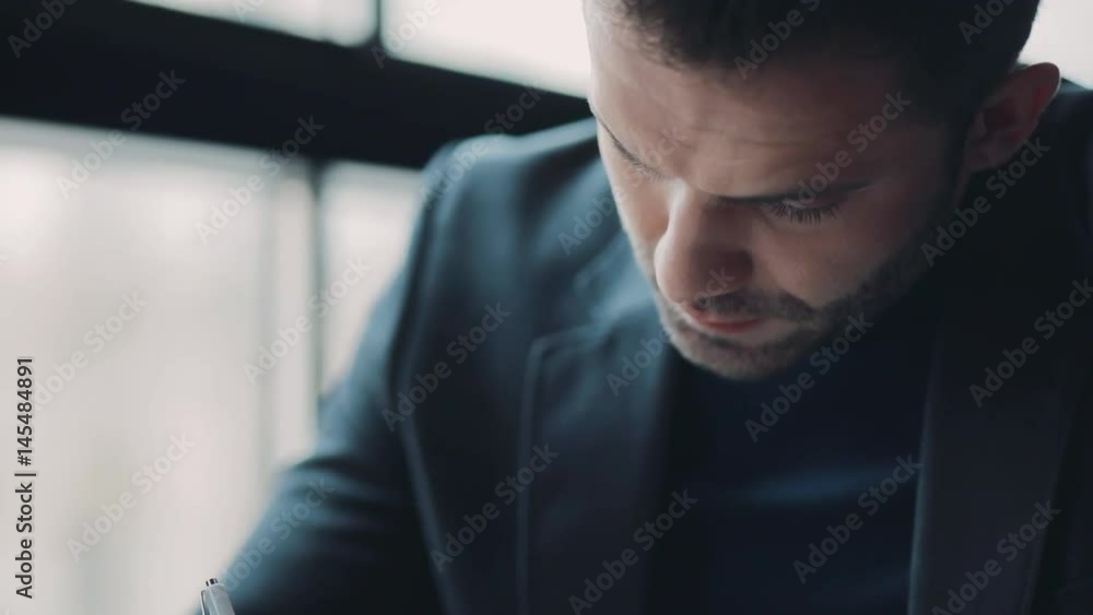 A young European man thinking, and taking notes in the café by the window. Formal wear. Business life, successful lifestyle. Males club, men’s style.