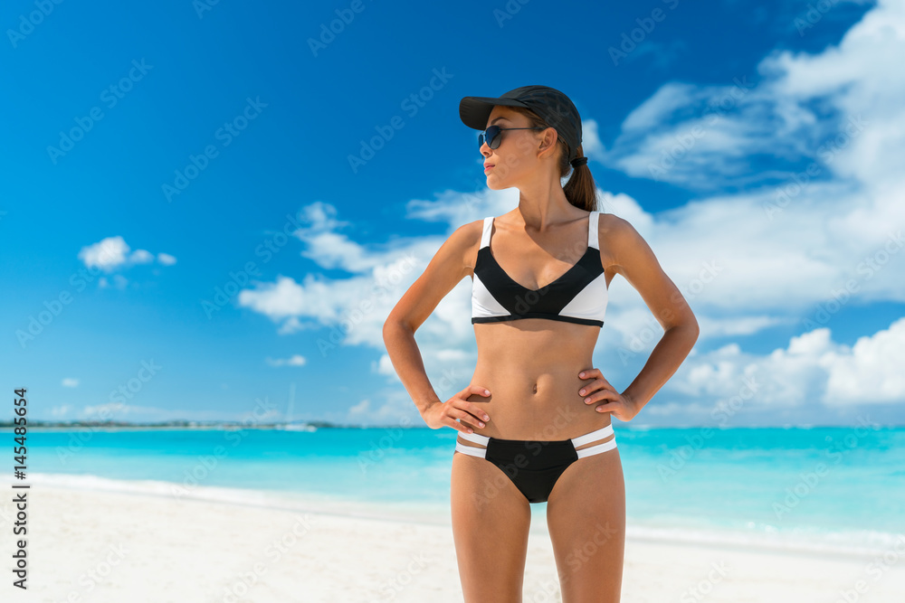 Sport beach woman ready for the summer season. Bikini fitness woman with sun protection hat and sunglasses tanning showing weight loss body on vacation.