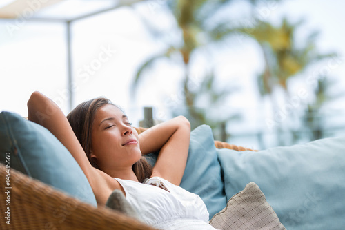Home lifestyle woman relaxing sleeping on sofa on outdoor patio living room. Happy lady lying down on comfortable pillows taking a nap for wellness and health. Tropical vacation. photo