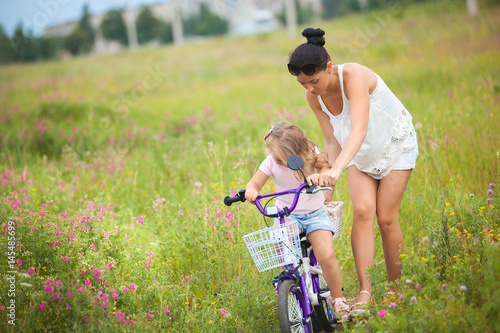 Young beautiful mother teaching her little daughter to ride a bike in the field. Mom and cute girl having fun together