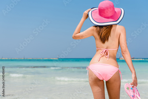 Beach vacation. Hot beautiful woman in sunhat and bikini standing with her arms raised to her head enjoying looking view of beach ocean on hot summer day. Photo from Hapuna beach, Big Island, Hawaii. photo
