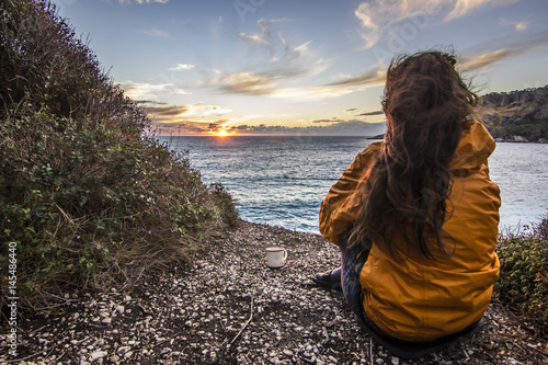 girl in yellow jacket sitting near seashore at sunset