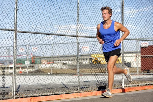 Runner man running - urban city lifestyle. Young sports male athlete jogging in grunge fence background outdoors in summer activewear. Active living.