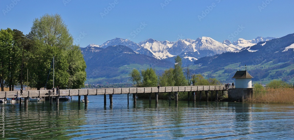 Springtime in Rapperswil. Gangplank on lake Zurichsee. Green trees and snow capped mountains.