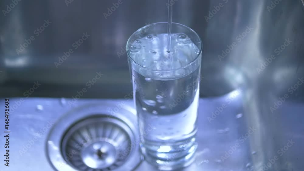 Pure water is poured into a glass, in the kitchen, in the sink. Pure water is poured into a glass, in the kitchen, in the sink.
