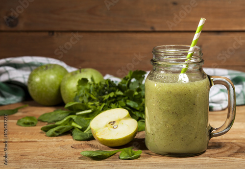 Freshly blended green smoothie in glass jar with straw. Wooden background.
