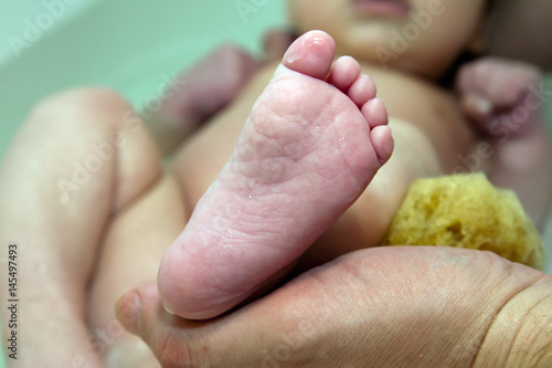 Mom keeps the heel of the baby while bathing photo