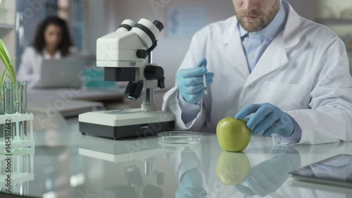 Lab assistant injecting apple with portion of pesticide for marketable condition