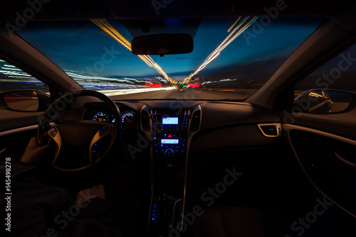 Hand on the wheel, one-handed operation. The car moves at a fast speed in the night of snooker. Blurred road with lights with a car at high speed