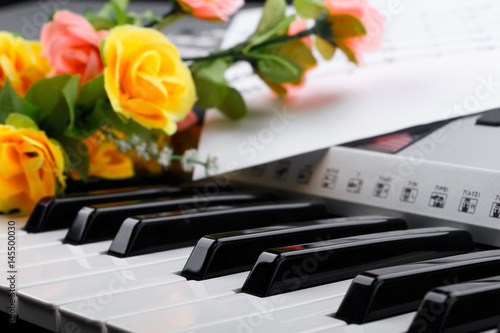 Fragment of electronic synthesizer keyboard with flowers and music notes sheets