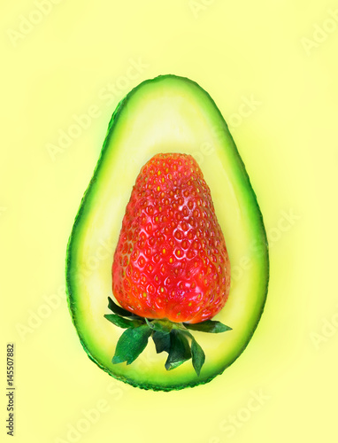 Creative mix of two fruits slices of avocado and strawberry on yellow green background. Art food concept