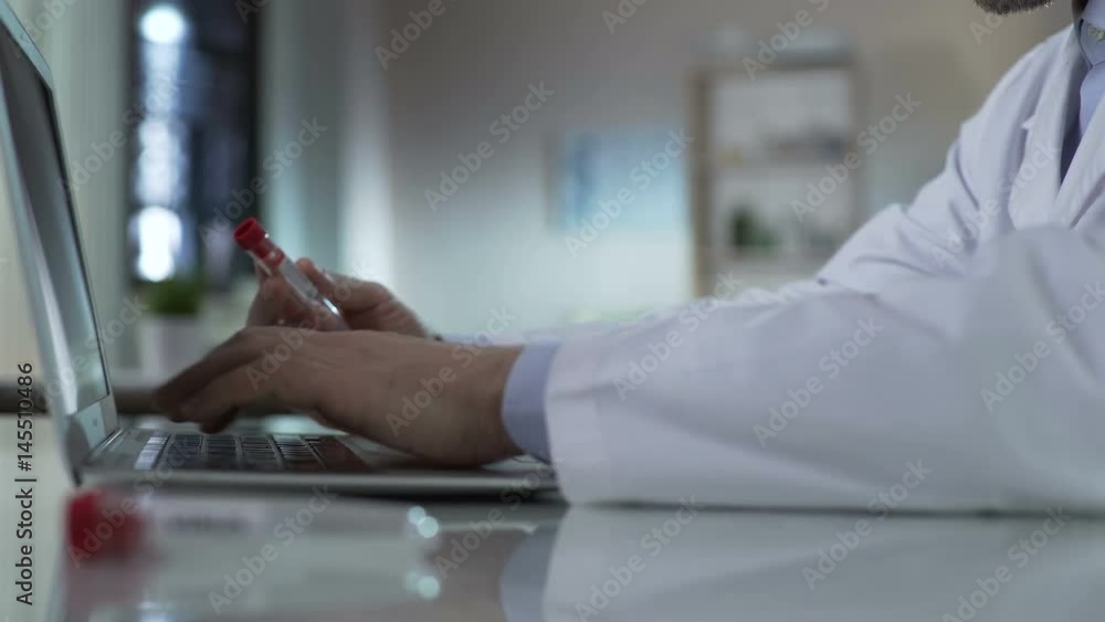Doctor typing information from test tube, adding results to medical record, lab Doctor typing information from test tube, adding results to medical record, lab