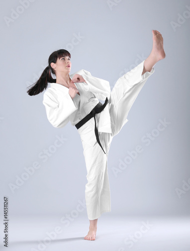Young sporty woman practicing martial arts on light background