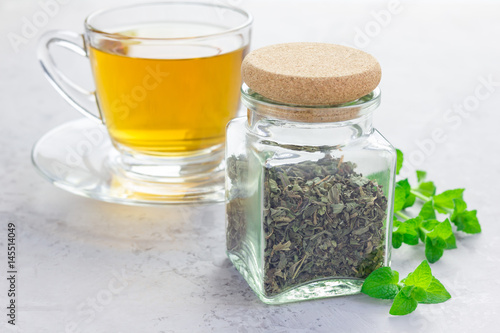 Dry herbal mint tea in a jar with cup of tea on background, horizontal